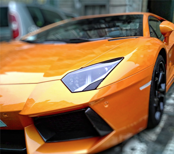 Close-up of an orange sports car's front headlight and sleek design.