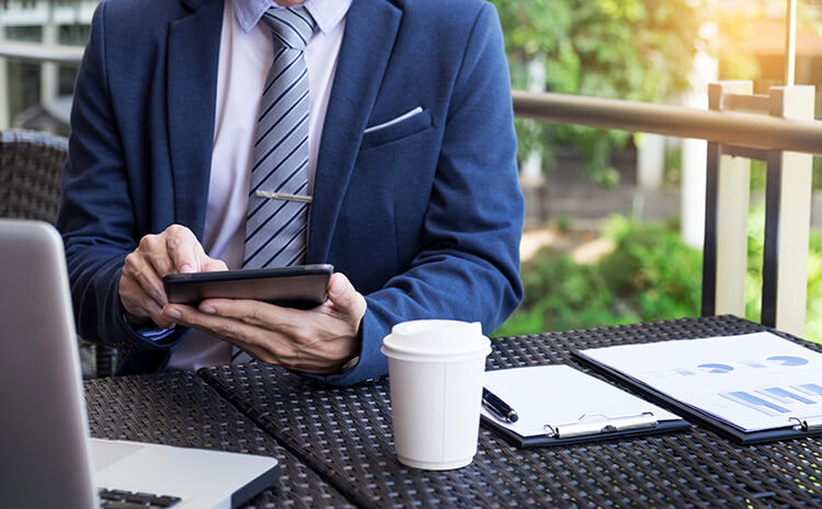 Businessman in a suit using a tablet at an outdoor café table.