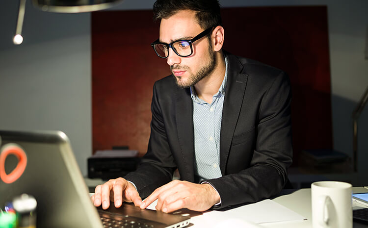 A focused man in glasses working on a laptop at a desk.